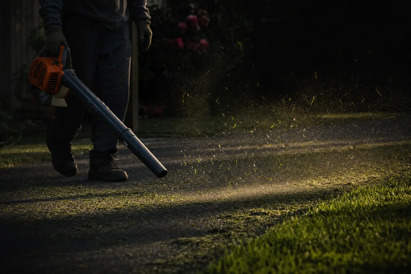 Grass clippings being blown off a residential driveway at dusk
