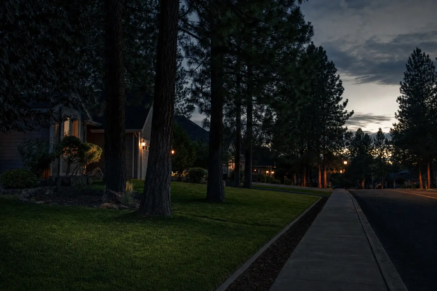 Tree-lined residential street in the Spokane area at dusk with neatly cut front lawns
